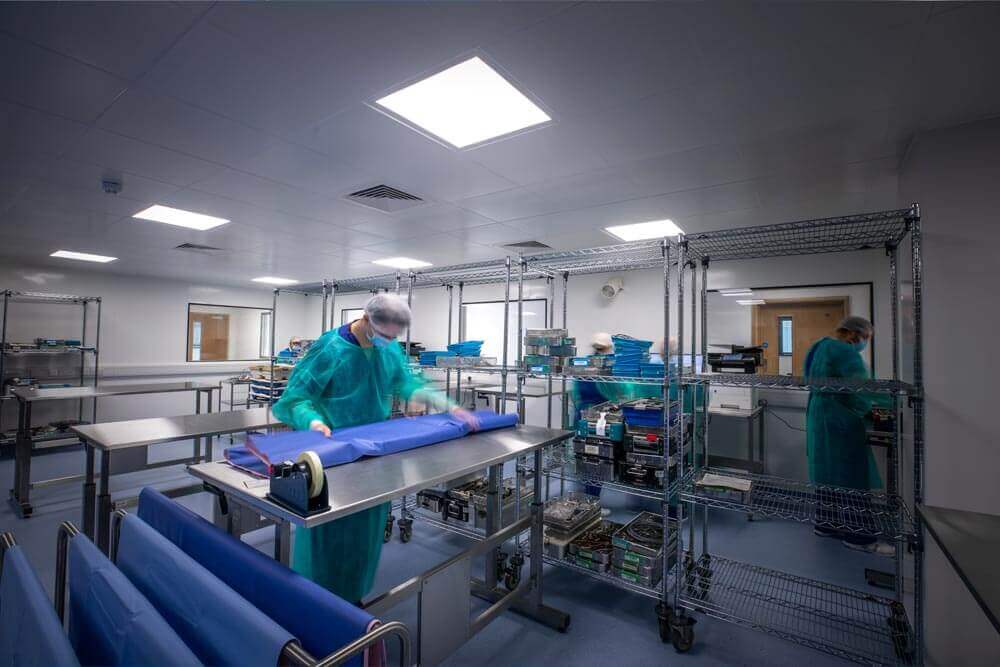 Workers busy sterlising medical tools in a storeroom, lined with sanitary surface covers over steel tables, and metal racks.